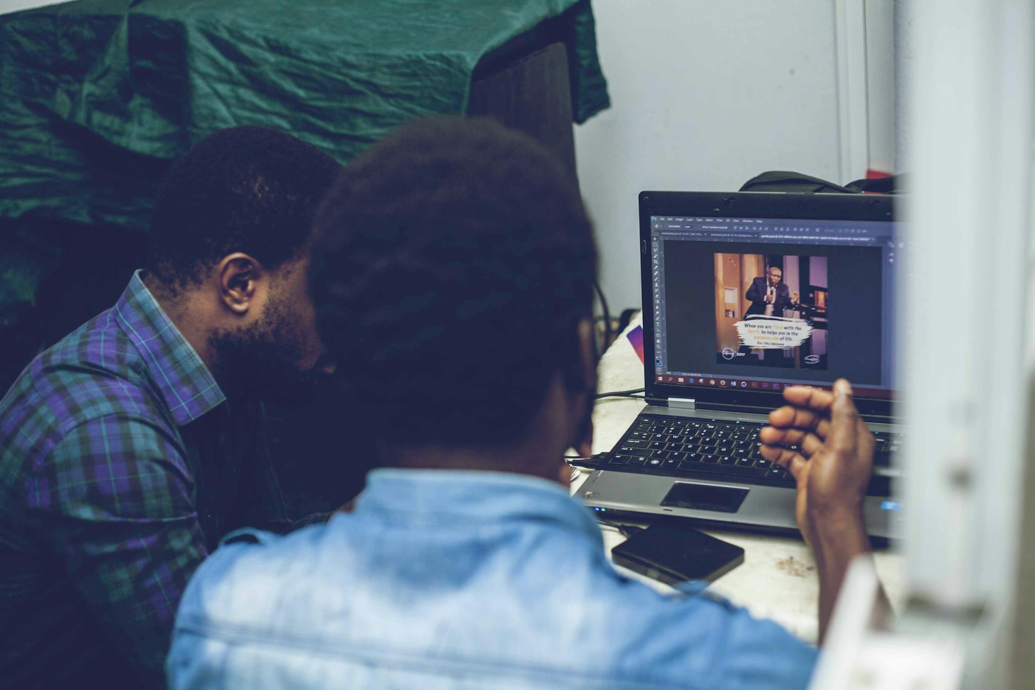 Two men collaborating on graphic design using a laptop indoors, focusing on technology and teamwork.